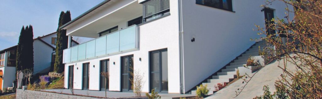 Hanghaus von der Seite mit weißer Fassade und Glasbalkon